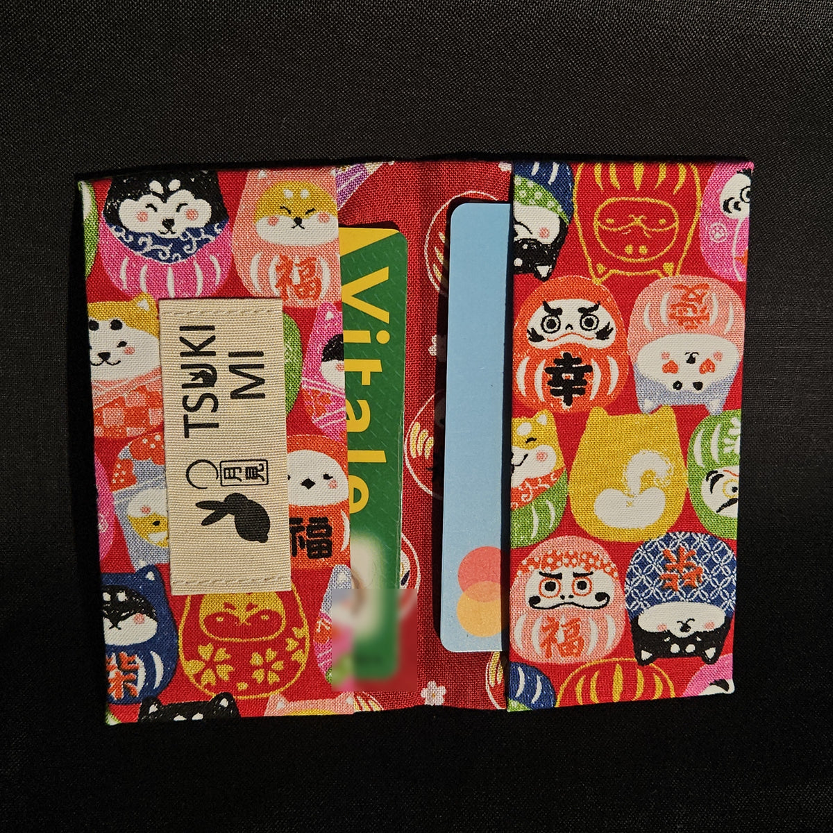 Porte-cartes Tsukimi darumas et shiba sur fond rouge, ouvert avec deux cartes glissées dans les compartiments