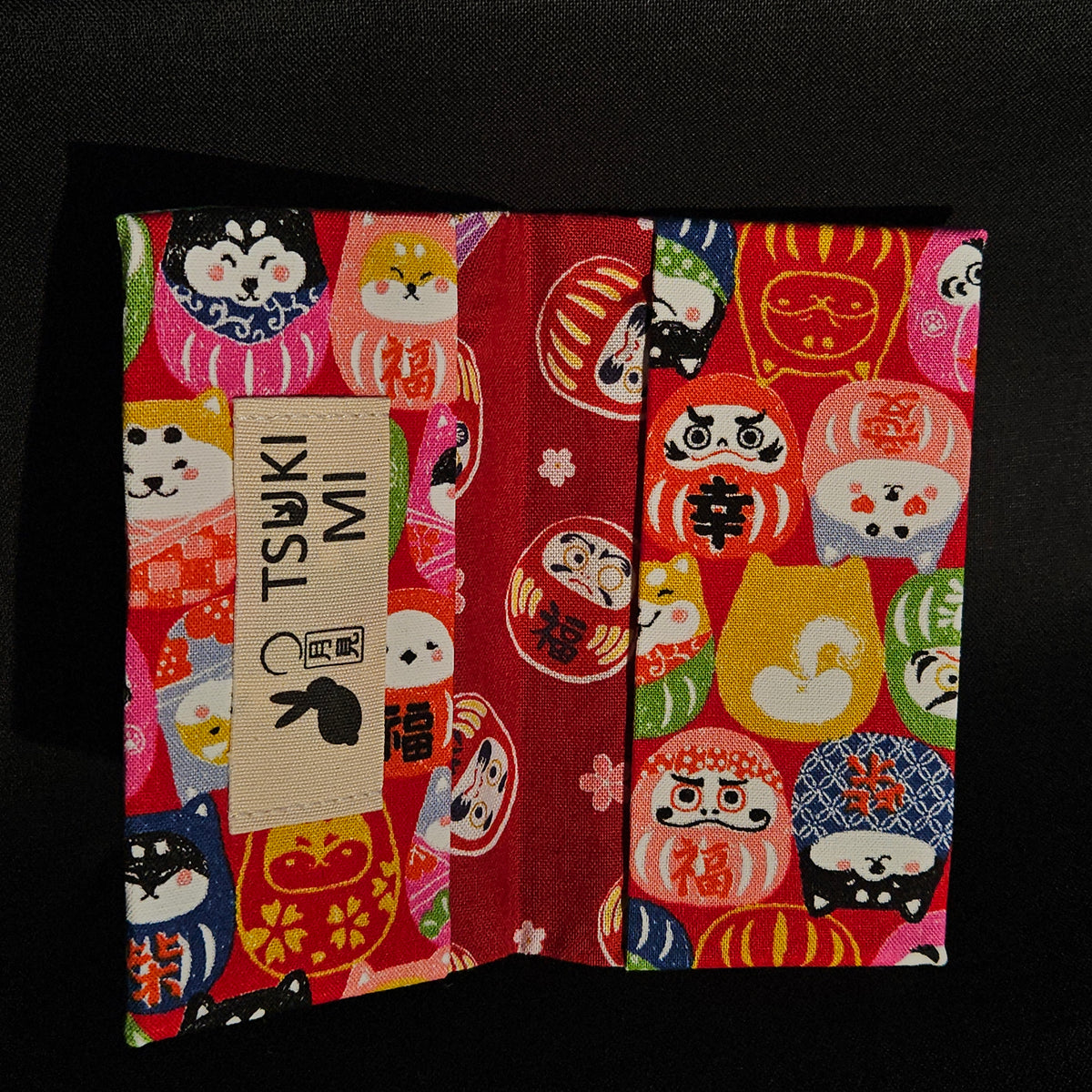 Porte-cartes Tsukimi ouvert : extérieur darumas et shiba sur fond rouge, intérieur rouge foncé à darumas et fleurs de cerisier
