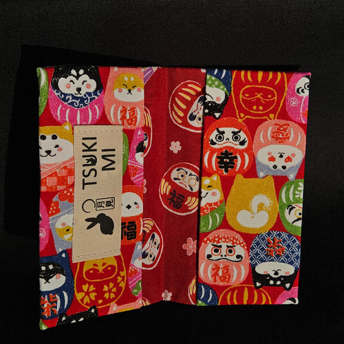 Porte-cartes Tsukimi ouvert : extérieur darumas et shiba sur fond rouge, intérieur rouge foncé à darumas et fleurs de cerisier