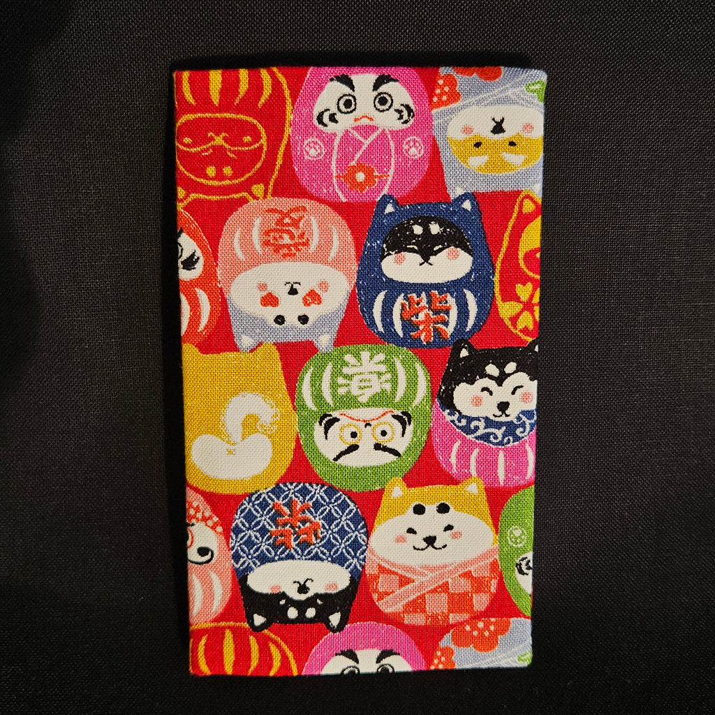 Porte-cartes Tsukimi fermé, en tissu japonais à petits darumas et shiba inu colorés, motif dense sur fond rouge