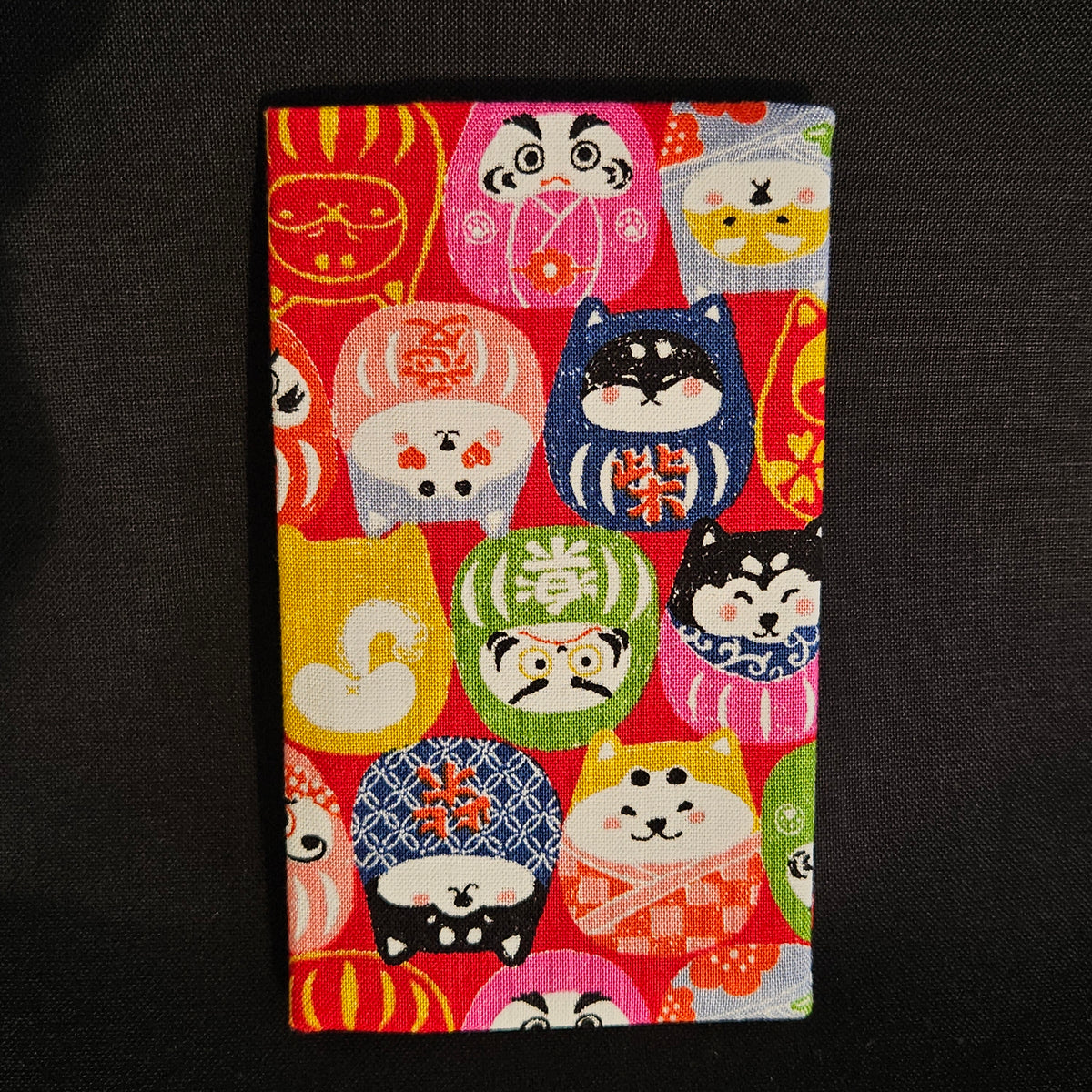 Porte-cartes Tsukimi fermé, en tissu japonais à petits darumas et shiba inu colorés, motif dense sur fond rouge