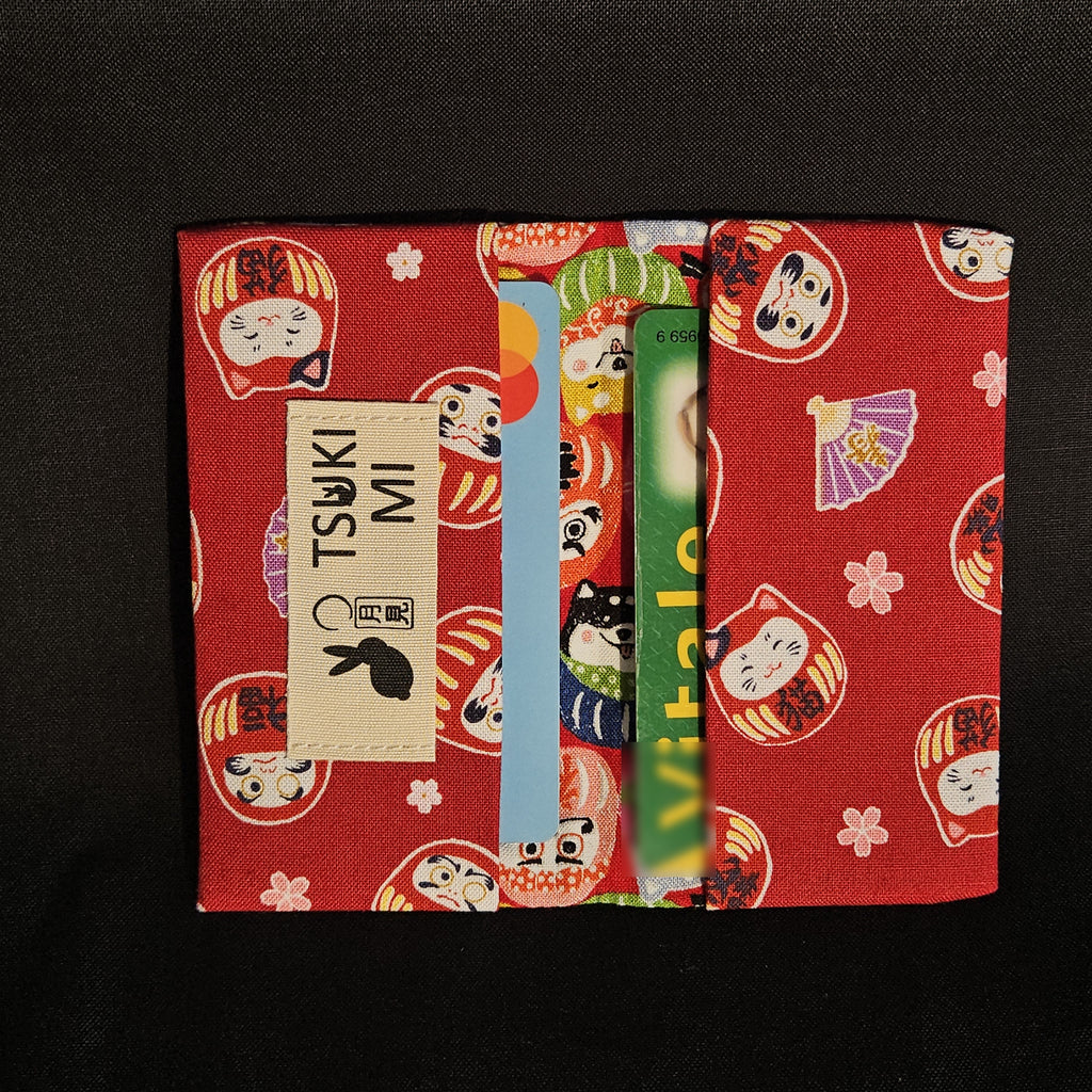 Porte-cartes Tsukimi darumas et shiba sur fond rouge vif, ouvert avec deux cartes glissées dans les compartiments