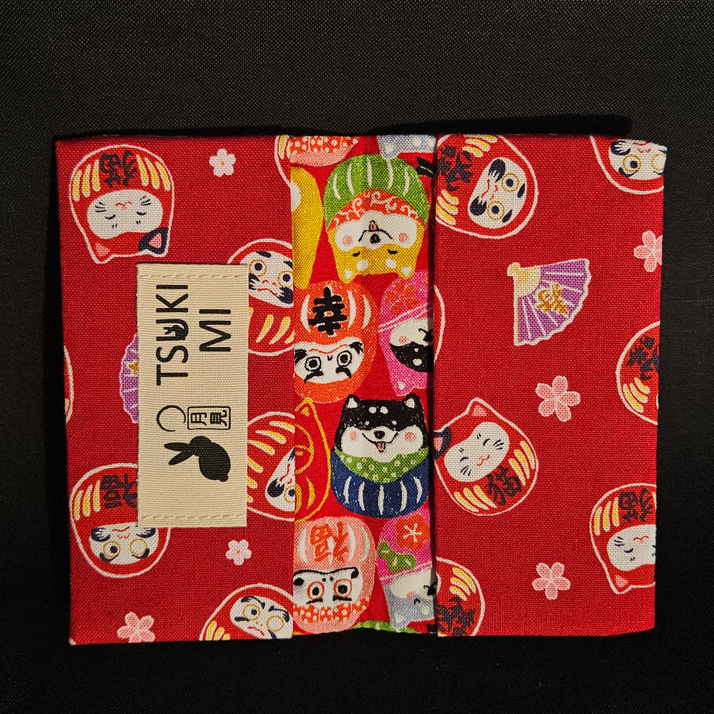 Porte-cartes Tsukimi ouvert : extérieur darumas et shiba colorés, intérieur rouge foncé à darumas et fleurs de cerisier