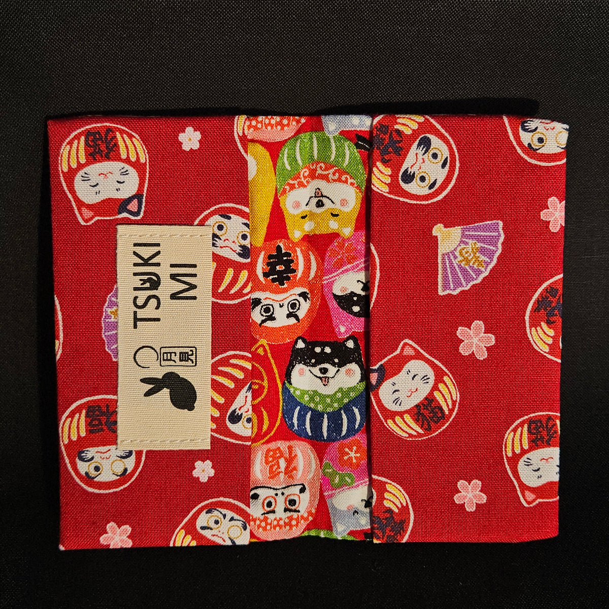 Porte-cartes Tsukimi ouvert : extérieur darumas et shiba colorés, intérieur rouge foncé à darumas et fleurs de cerisier